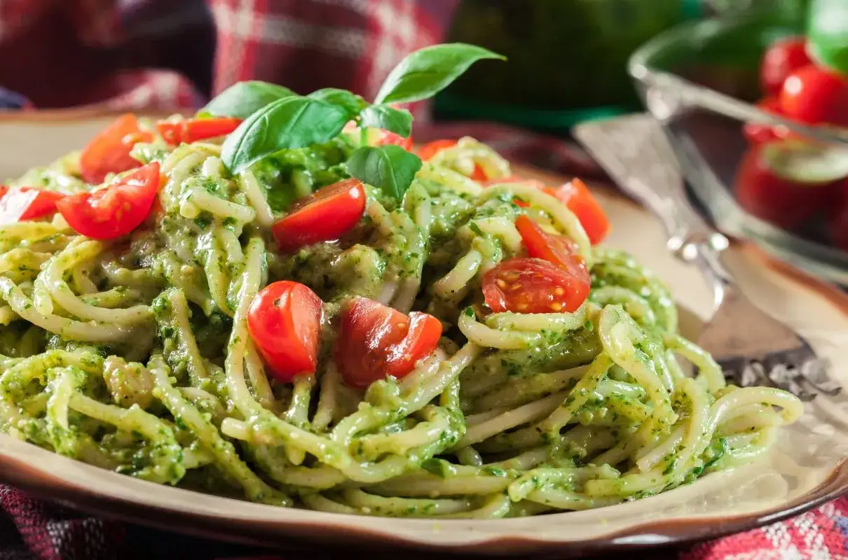 Pyszne spaghetti z kremowym sosem, czyli pasta z awokado, ozdobiona pomidorkami koktajlowymi i listkami bazylii.