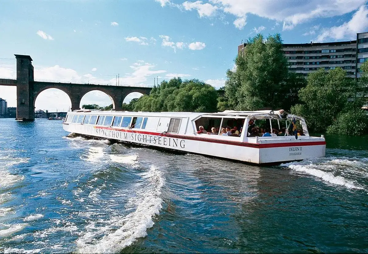 En sightseeingbåt passerar under en bro i Stockholm. Vattnet skummar bakom båten.