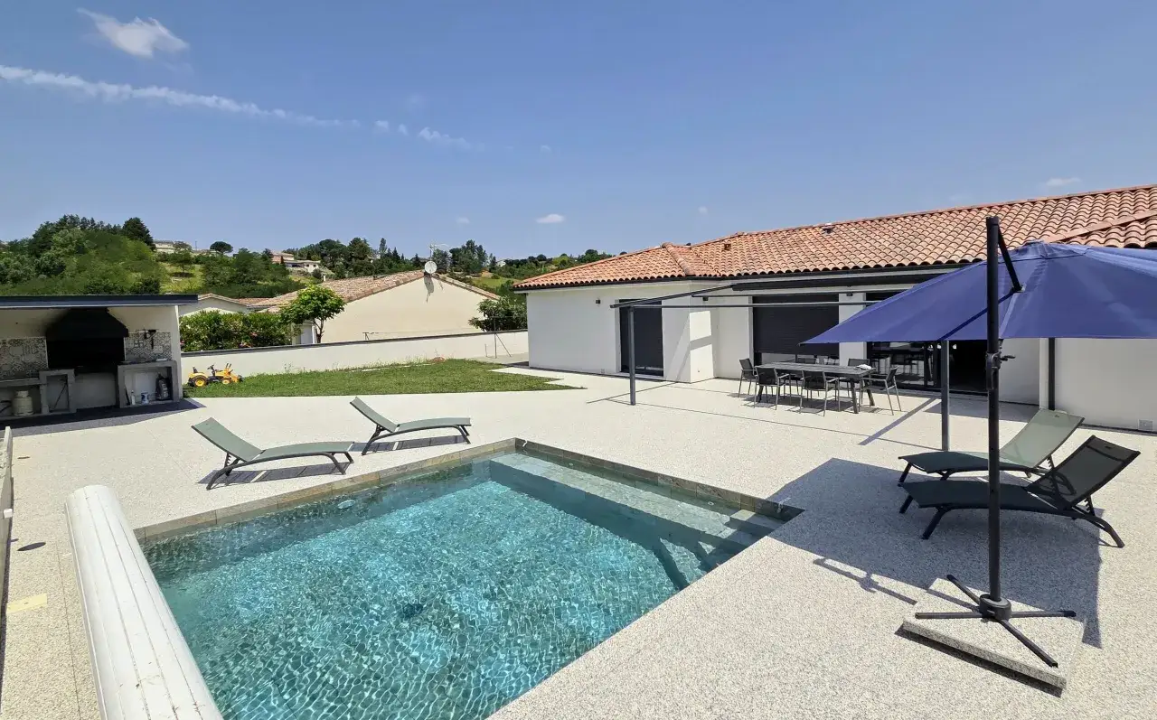 Un espace de détente avec une piscine entourée de béton ciré. Des chaises longues et un parasol invitent au repos.