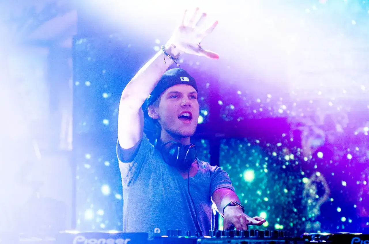 Avicii, DJ, wznosi rękę, jakby śpiewał