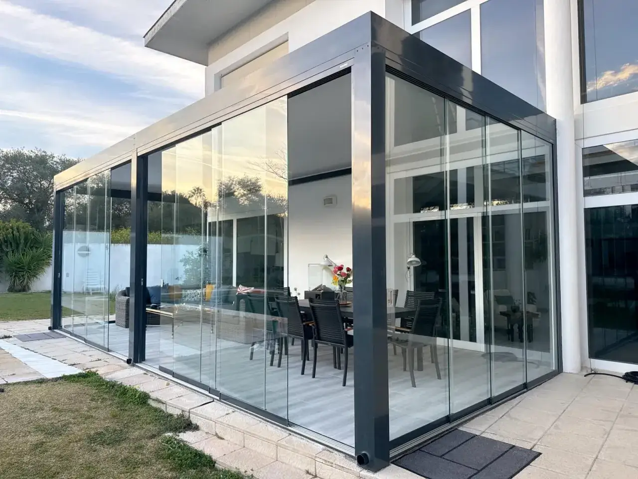 Modern glass enclosure to cerrar patio exterior, creating a bright dining and living space with views of the garden.