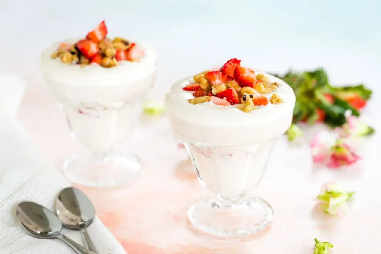 Zwei Gläser mit cremigem Joghurt, garniert mit frischen Erdbeeren und Granola. Ein leckerer Low-Carb-Genuss.