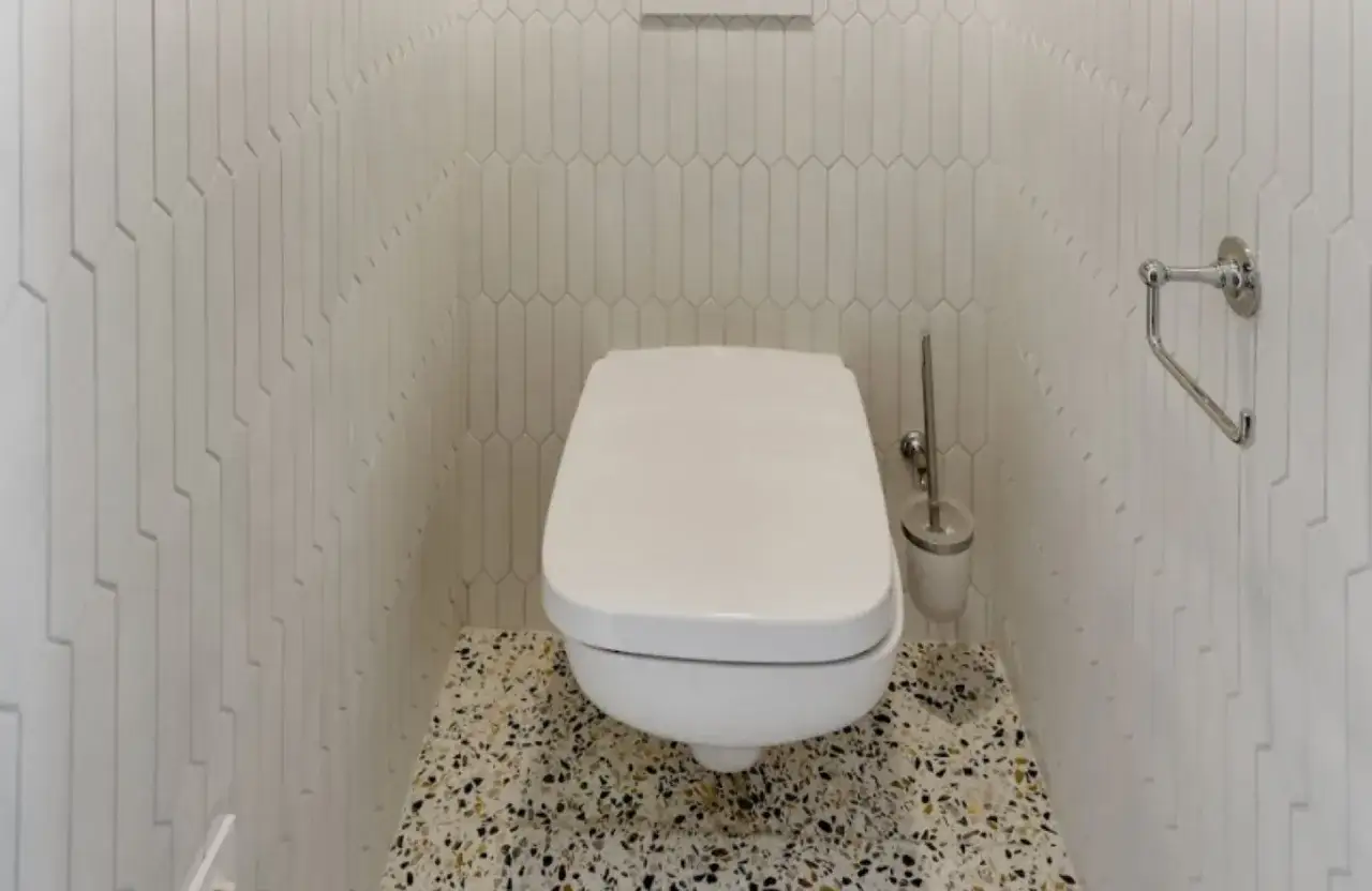 Une salle de bain moderne avec des carreaux blancs allongés et un sol en terrazzo coloré. Parfait pour refaire ses toilettes avec style.
