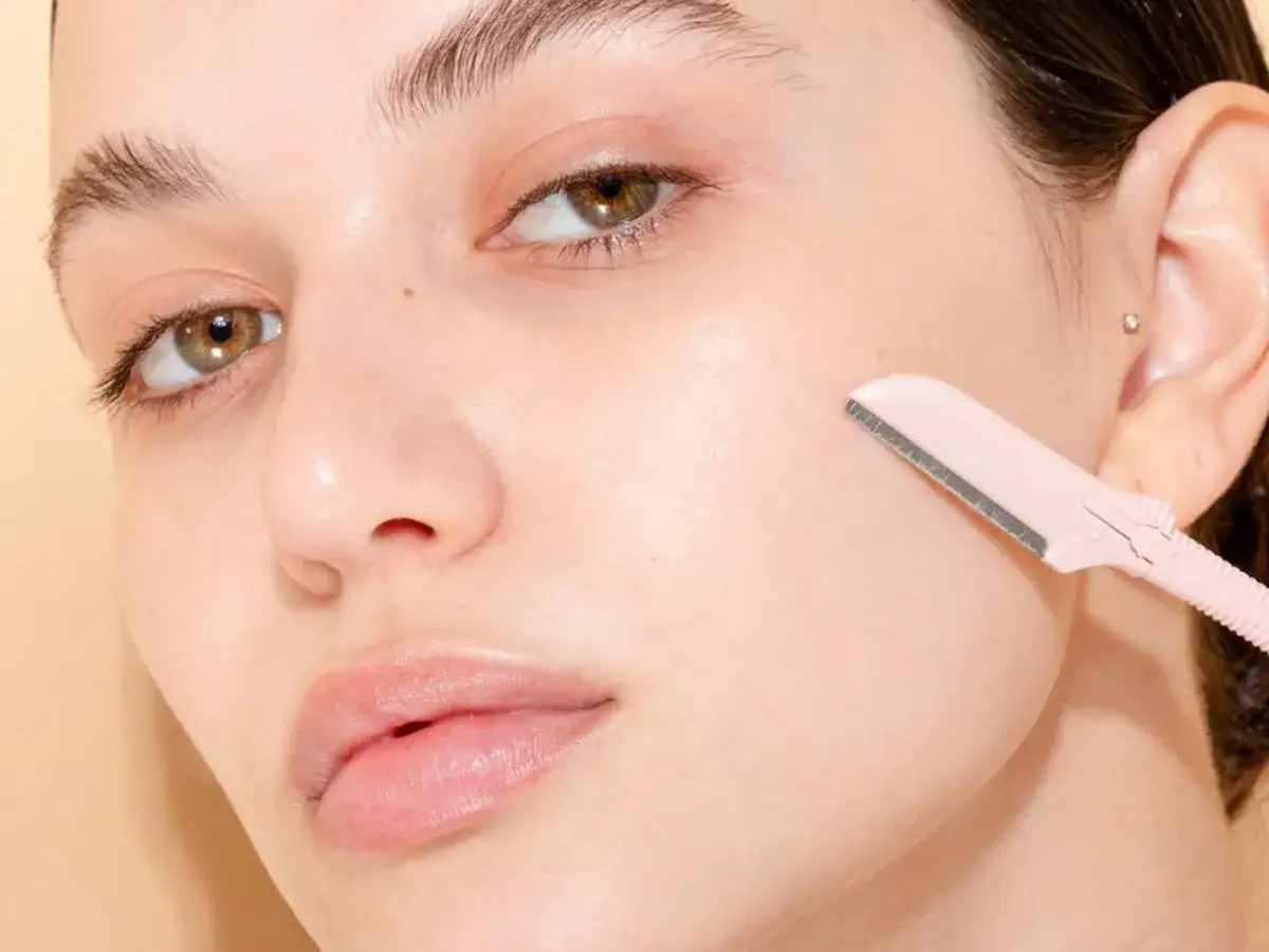 Mujer joven con piel radiante, usando una cuchilla para afeitado y depilaci&oacute;n facial.