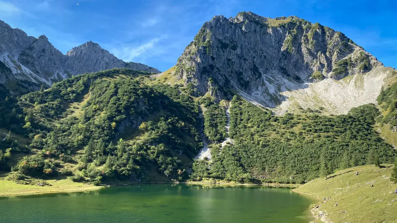 Gr&uuml;ner Bergsee vor steilen Felsw&auml;nden, ideal f&uuml;r eine rubihorn wanderung. Kleine Gruppe von Wanderern am Ufer.