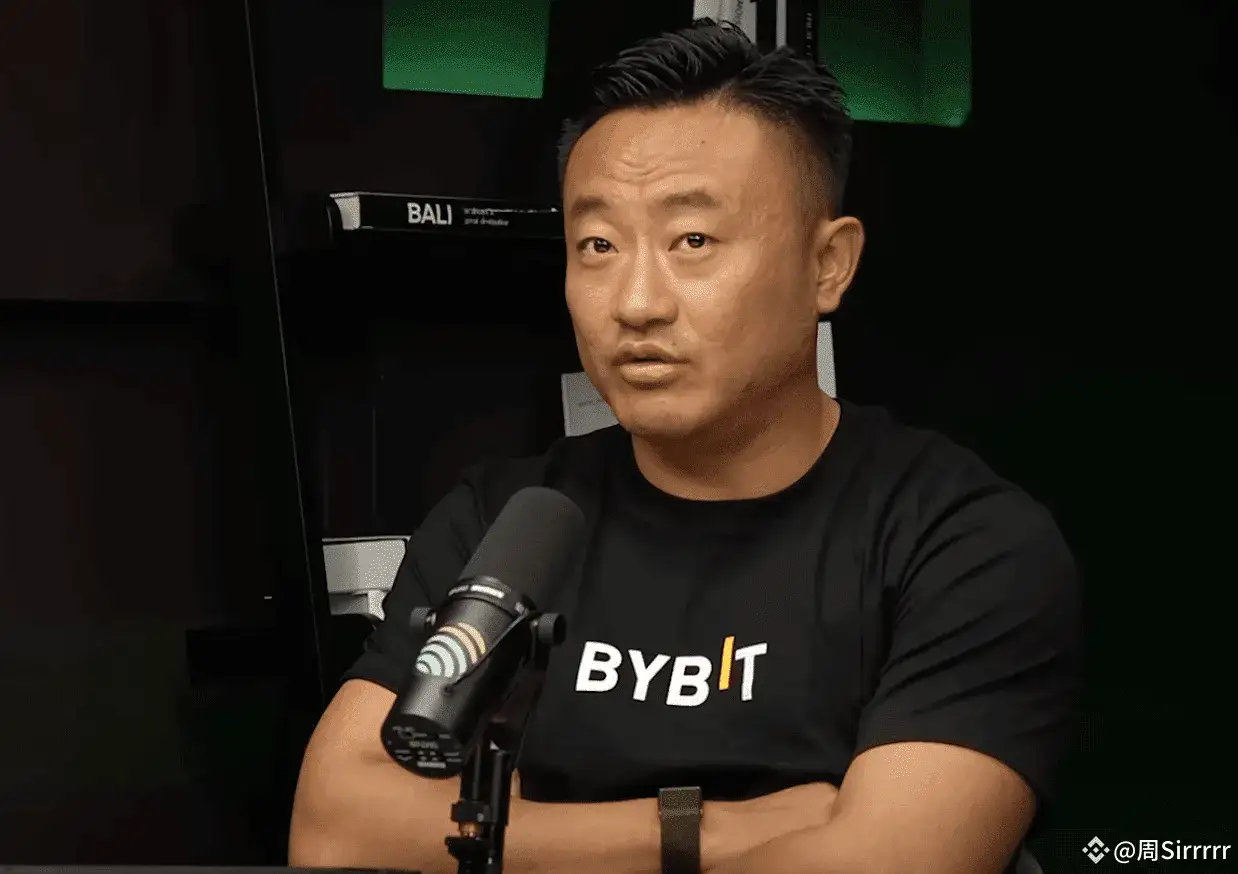 Ben Zhou w czarnej koszulce z logo Bybit, siedzi przed mikrofonem, opierając ręce na stole.