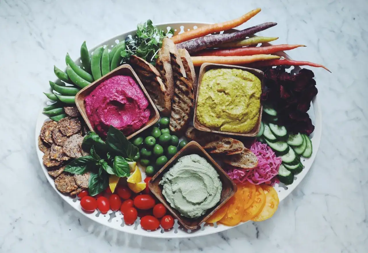 Buntes vegan party buffet mit drei Dips, Gemüse, Brot und Crackern.