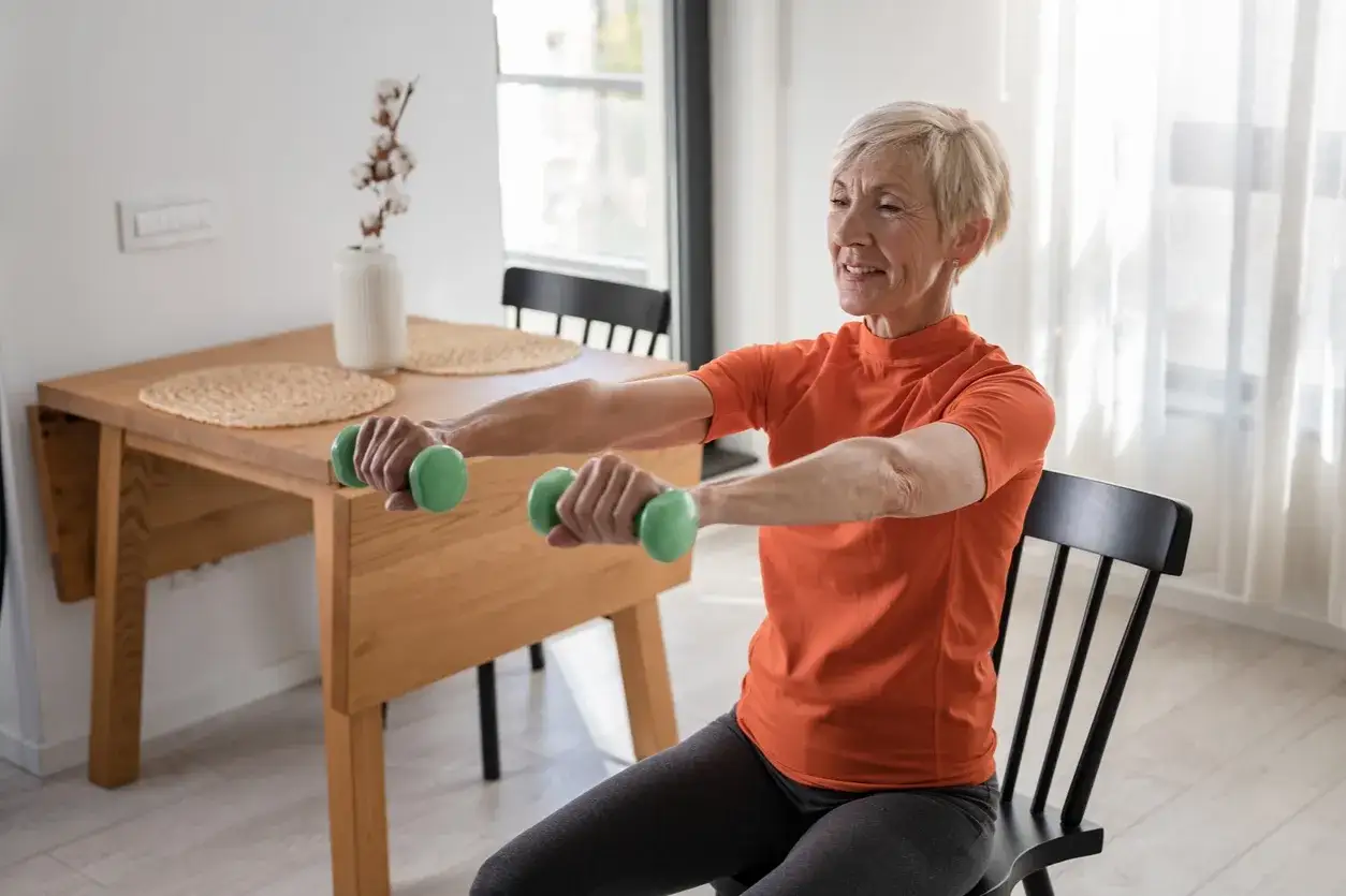 Femme souriante de 60 ans faisant des exercices avec haltères verts, une routine pour perdre du ventre après 60 ans.