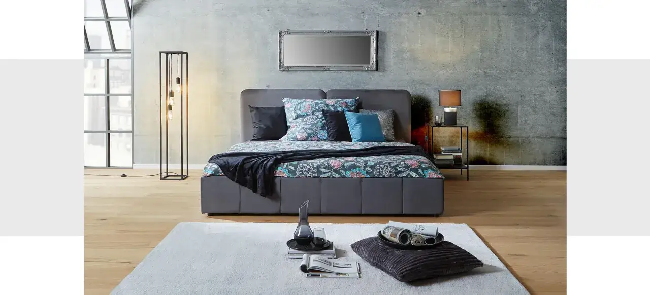 Stilvolles Schlafzimmer mit grauem Bett, floraler Bettw&auml;sche und moderner Beleuchtung. Tolle Schlafzimmer Ideen f&uuml;r ein gem&uuml;tliches Ambiente.