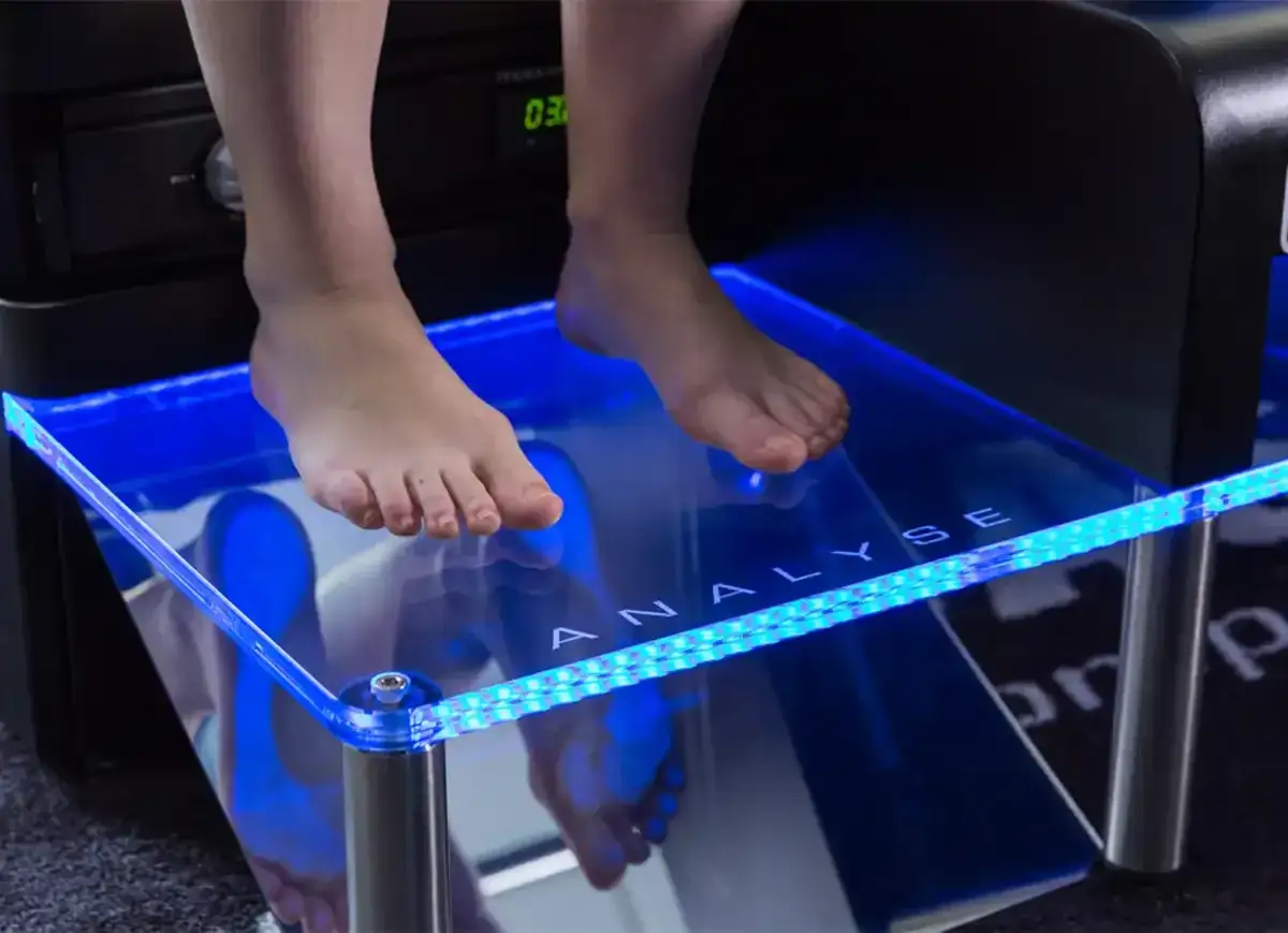 Pieds nus sur une plateforme d'analyse lumineuse bleue pour un examen de podologie.