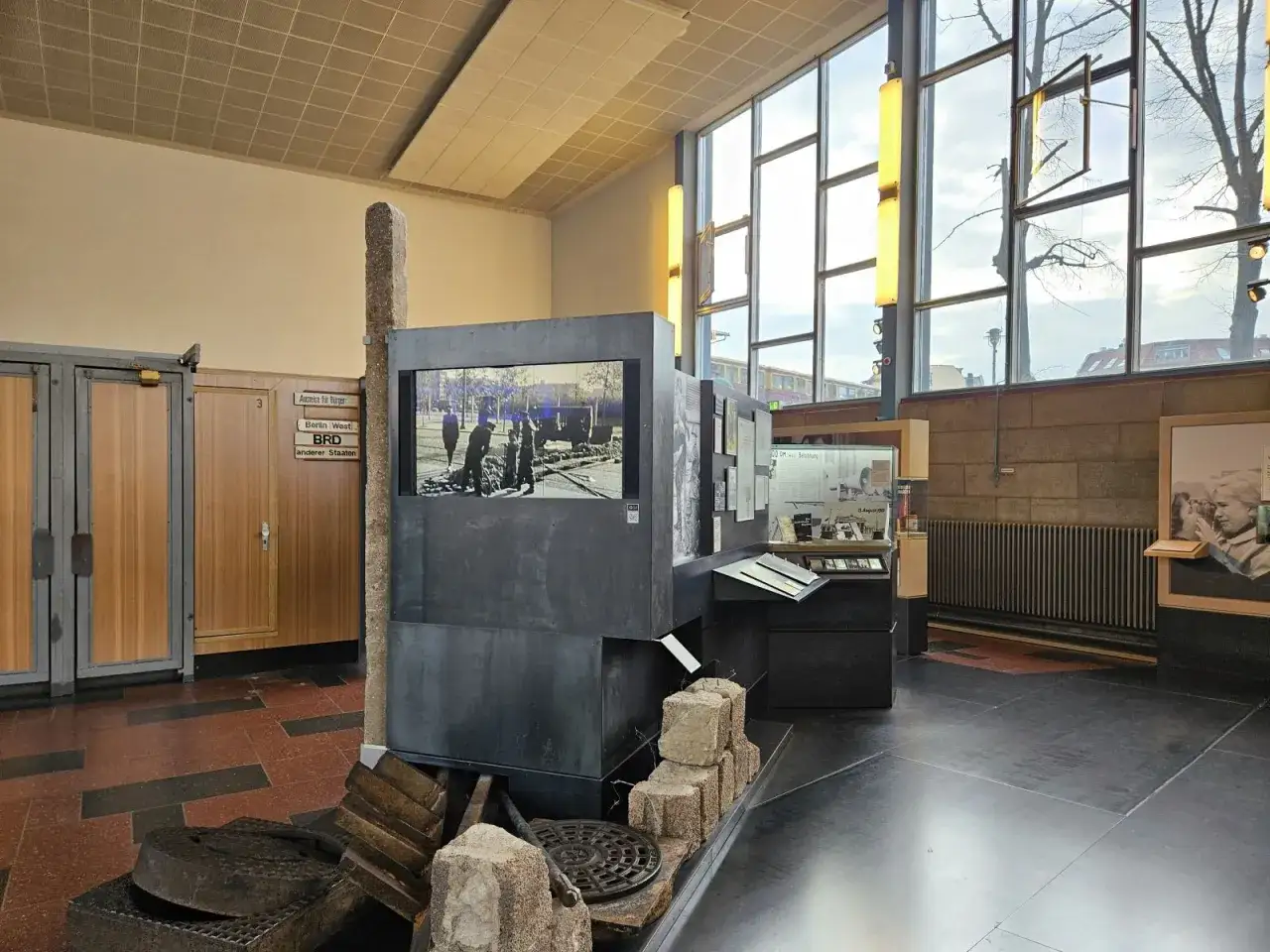 Ausstellung im **Palace of Tears Berlin**: Ein Stein, ein Bildschirm mit historischem Bild, Ausstellungsst&uuml;cke und Fensterfront.
