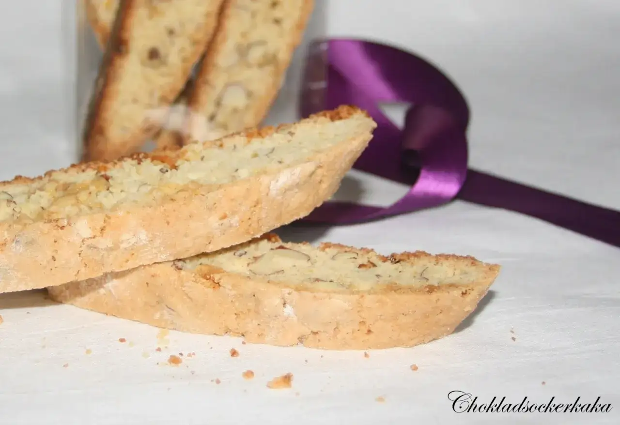 Tv&aring; mandel-biscottis ligger p&aring; en vit duk, med en lila sidenband i bakgrunden. Ett perfekt recept p&aring; biscotti!
