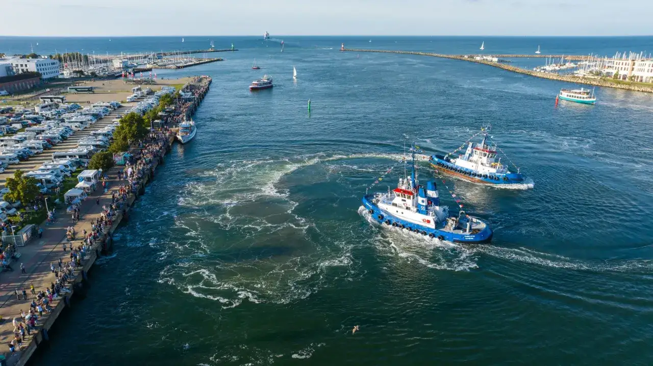 Zwei Schlepper drehen Pirouetten im Wasser, während am Kai viele Menschen das maritime Festival in Rostock bestaunen.