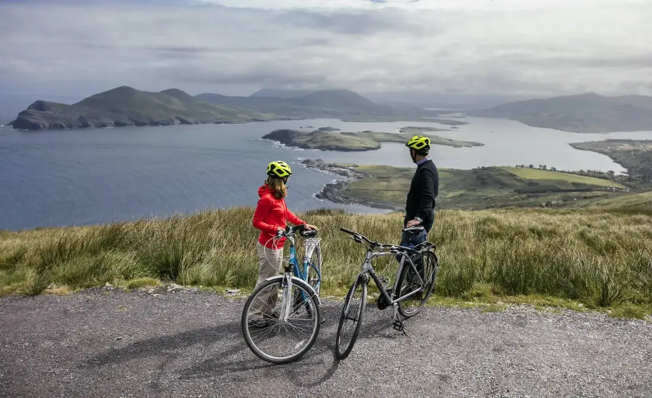 Pareja disfrutando de un paseo en bicicleta por la costa de Irlanda, con vistas a islas y montañas.