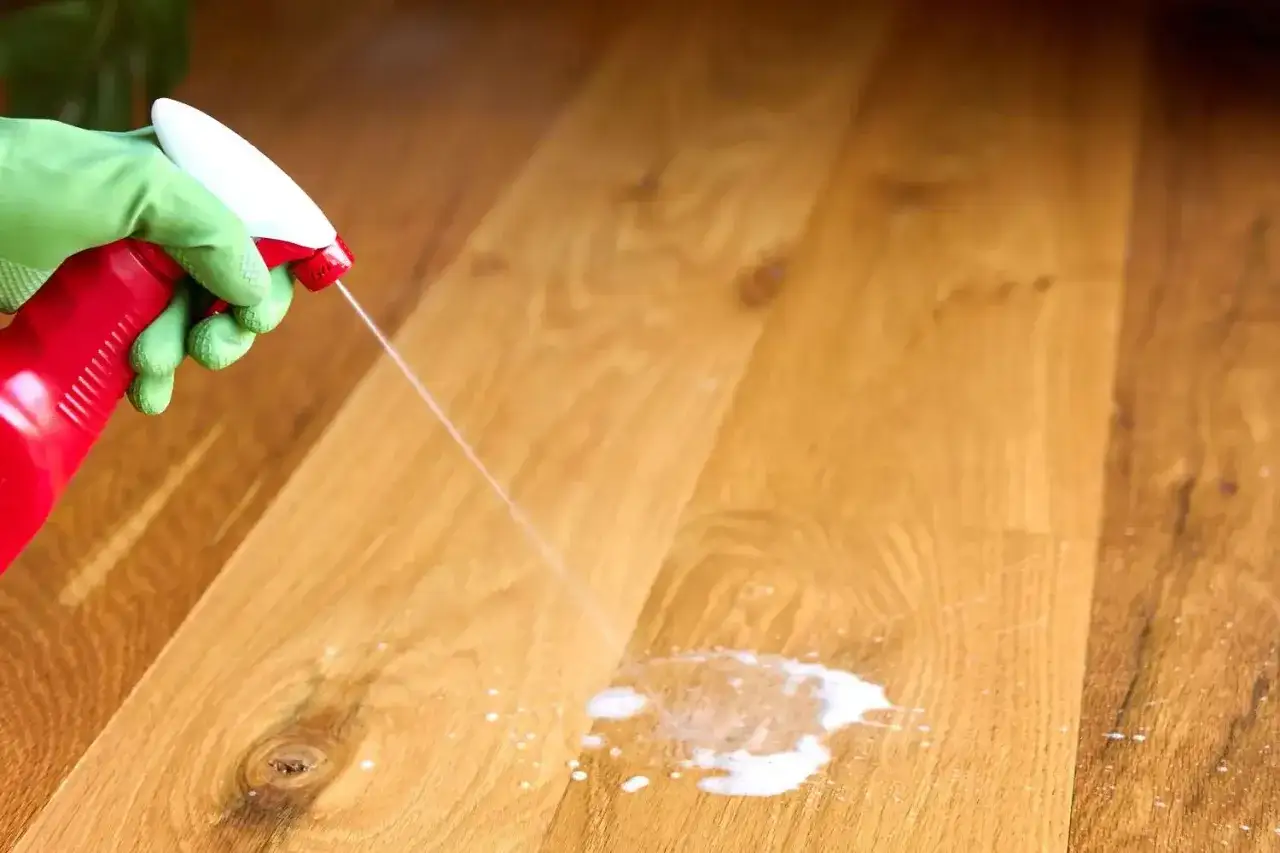 Main verte pulvérisant un produit pour enlever tache urine sur parquet bois.