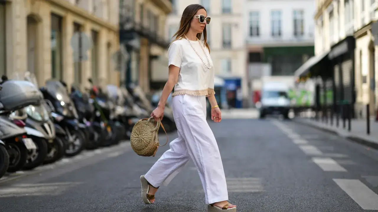 Mujer con un outfit blanco y alpargatas, paseando por la calle con una cesta de mimbre.