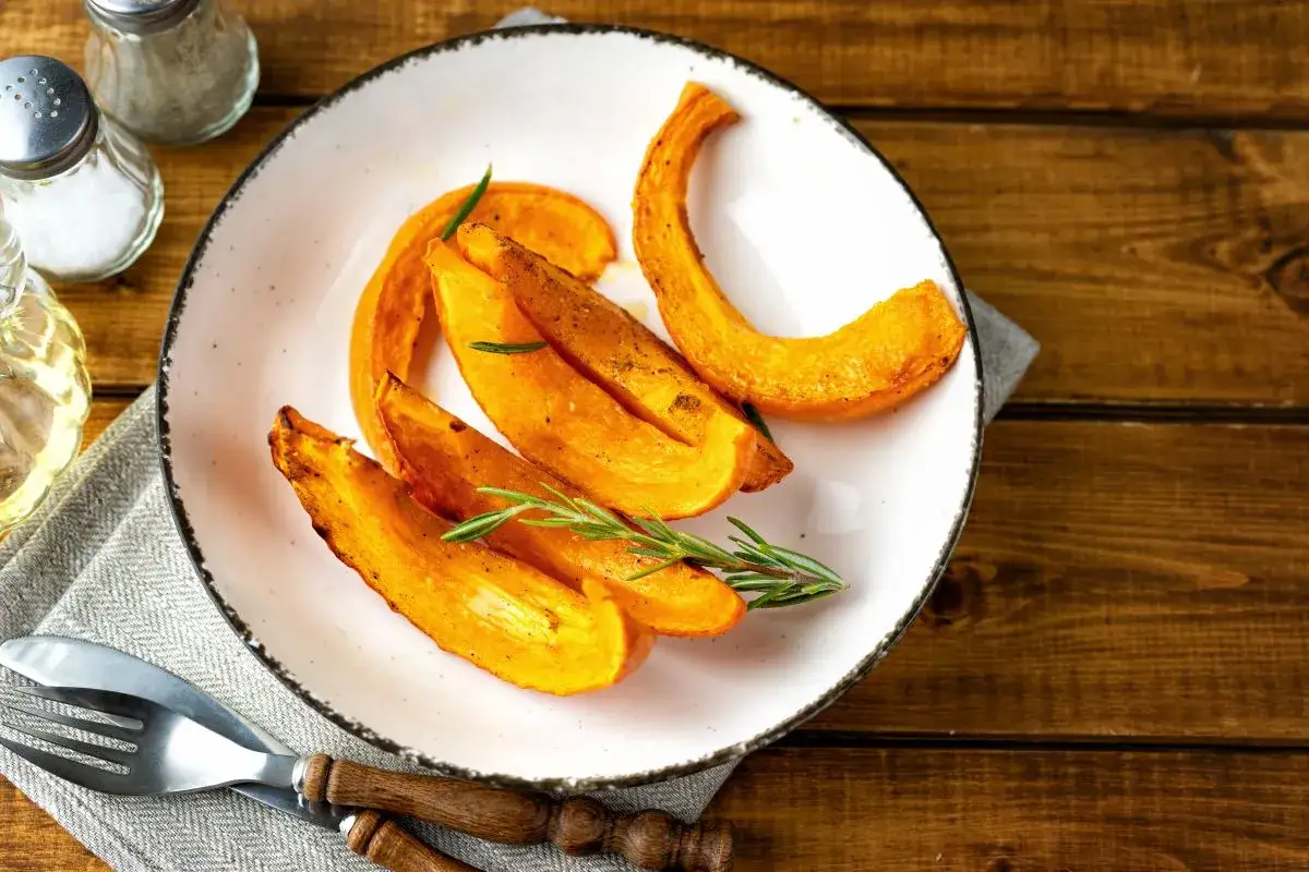 Fette di zucca dorate e profumate, cotte alla perfezione nella friggitrice ad aria, guarnite con rosmarino fresco su un piatto bianco.
