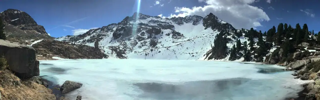 Panoramica del lago delle stellune ghiacciato, circondato da montagne innevate e rocce.