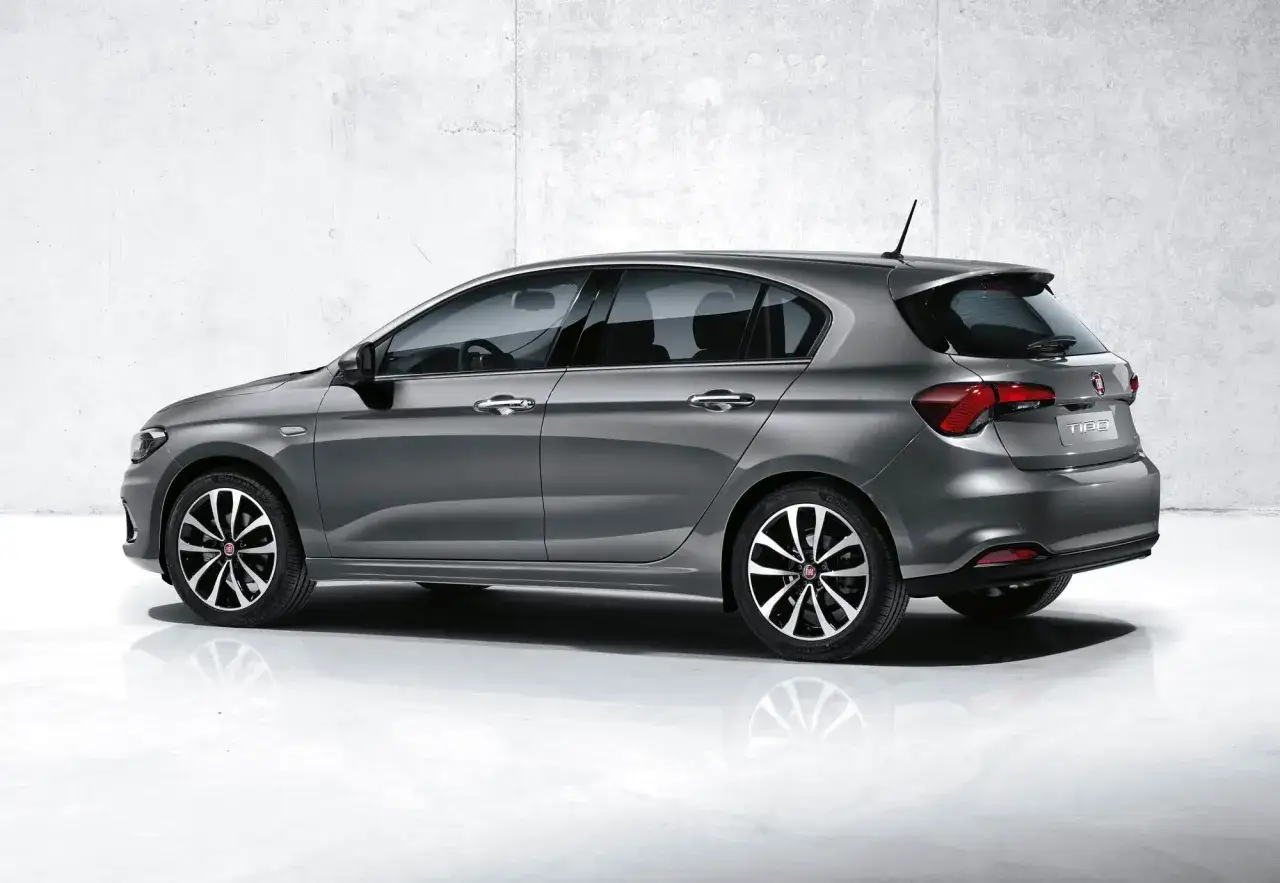 Grå Fiat Tipo, sedd från sidan och bakifrån, står på ett glänsande golv framför en betongvägg.