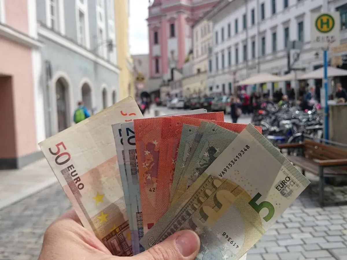 Dłoń trzyma banknoty euro, pokazując, jaka waluta jest w Austrii. W tle ulica miasta.