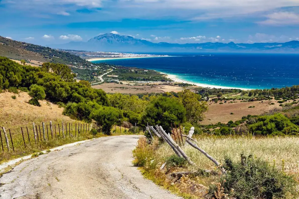 Camino rural con vistas a la costa de Tarifa, el mar azul y montañas al fondo. La tarifa como llegar es sencilla por esta ruta escénica.