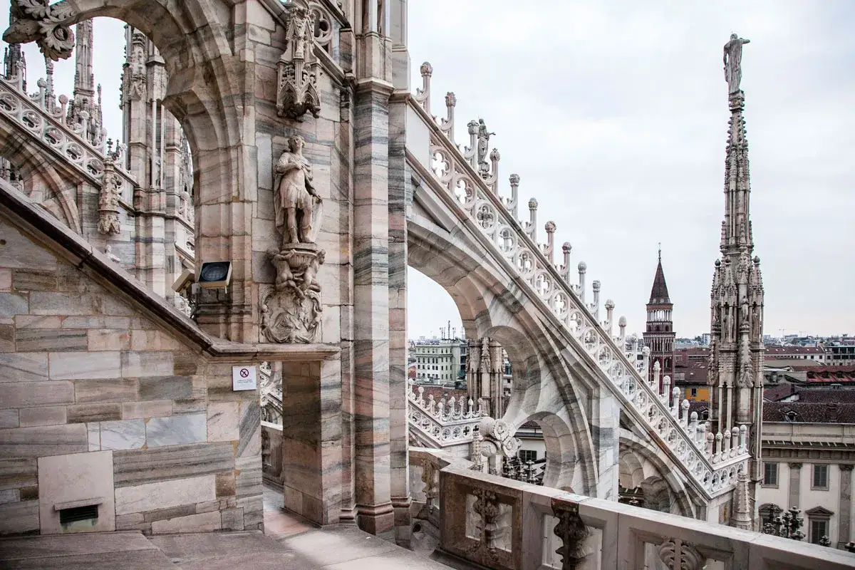 Dettaglio delle guglie e delle statue sui tetti del Duomo di Milano, con la citt&agrave; sullo sfondo.