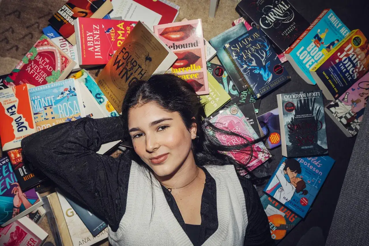En ung kvinna omgiven av böcker, bland annat titlar som antyder en passion för erotisk litteratur och spännande berättelser.