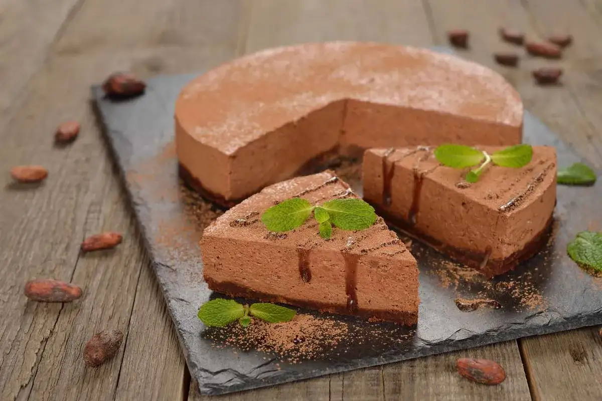 Una deliziosa bavarese al cioccolato, spolverata di cacao e decorata con menta fresca, su una lavagna scura con chicchi di cacao sparsi.