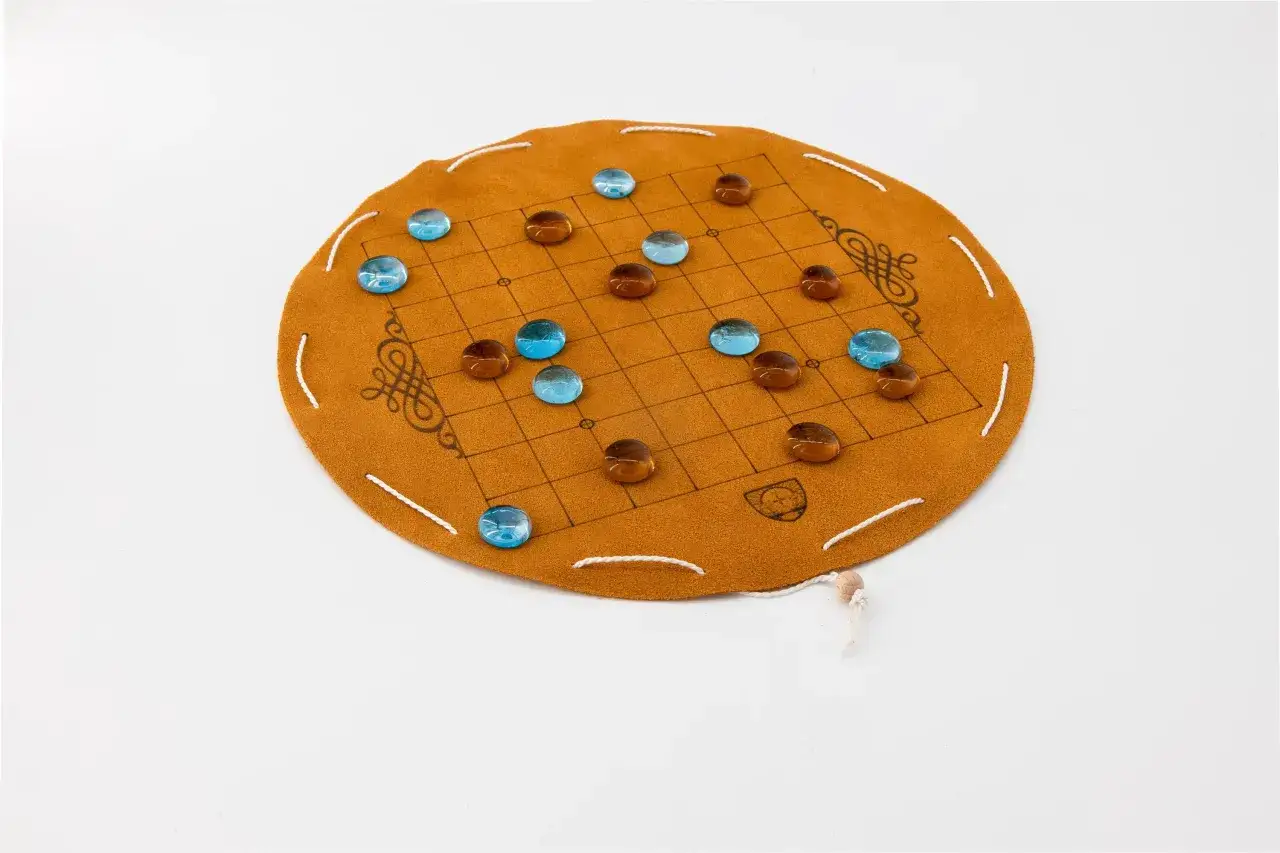 Rundes, braunes Brettspiel aus Leder mit einem Gittermuster und blauen und braunen Glassteinen. Ein Beispiel f&uuml;r japanische Brettspiele.