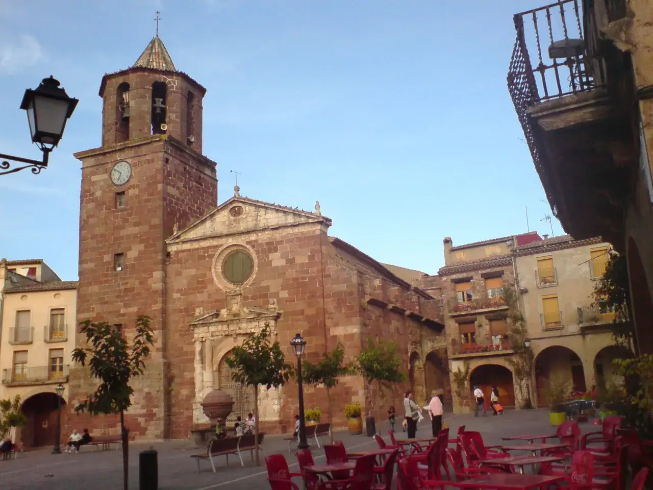 Plaza con iglesia de piedra y campanario, edificios históricos y mesas de terraza. Un buen lugar que ver en Prades para disfrutar del ambiente.