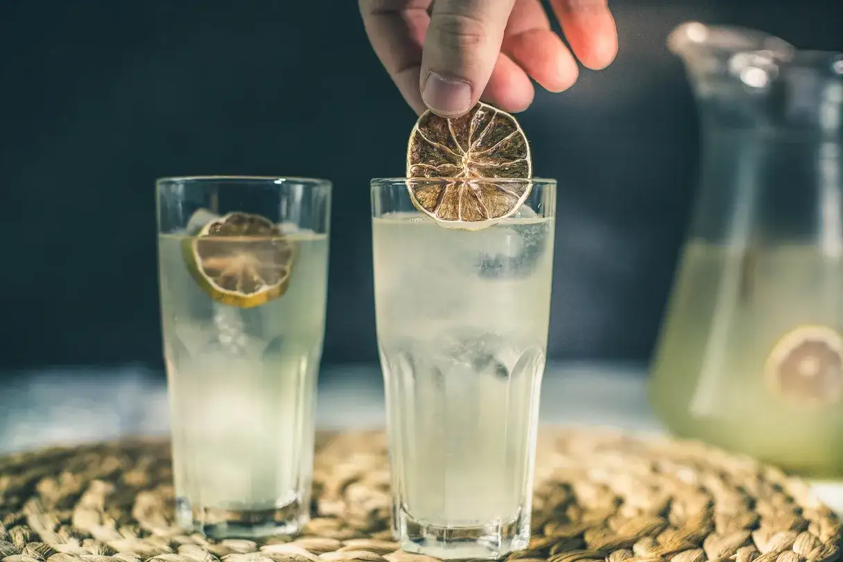 Domowy kordiał limonkowy o smaku jak z baru. Dwa szklanki orzeźwiającego napoju z lodem i plasterkiem limonki, w tle dzbanek z tym samym napojem.