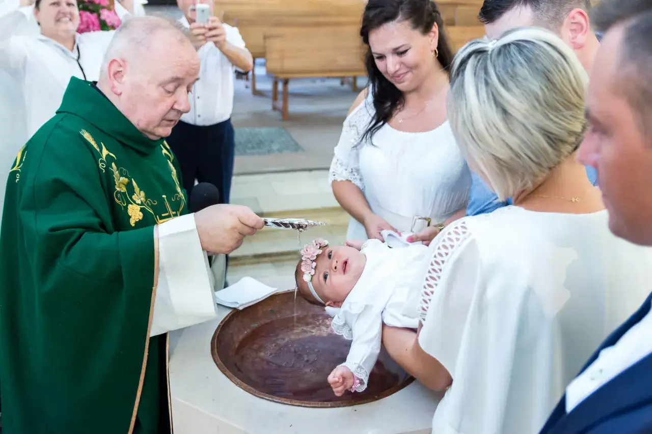 Kapłan polewa wodą głowę niemowlęcia w chrzcielnicy. Chrzest daje nowe życie w wierze.