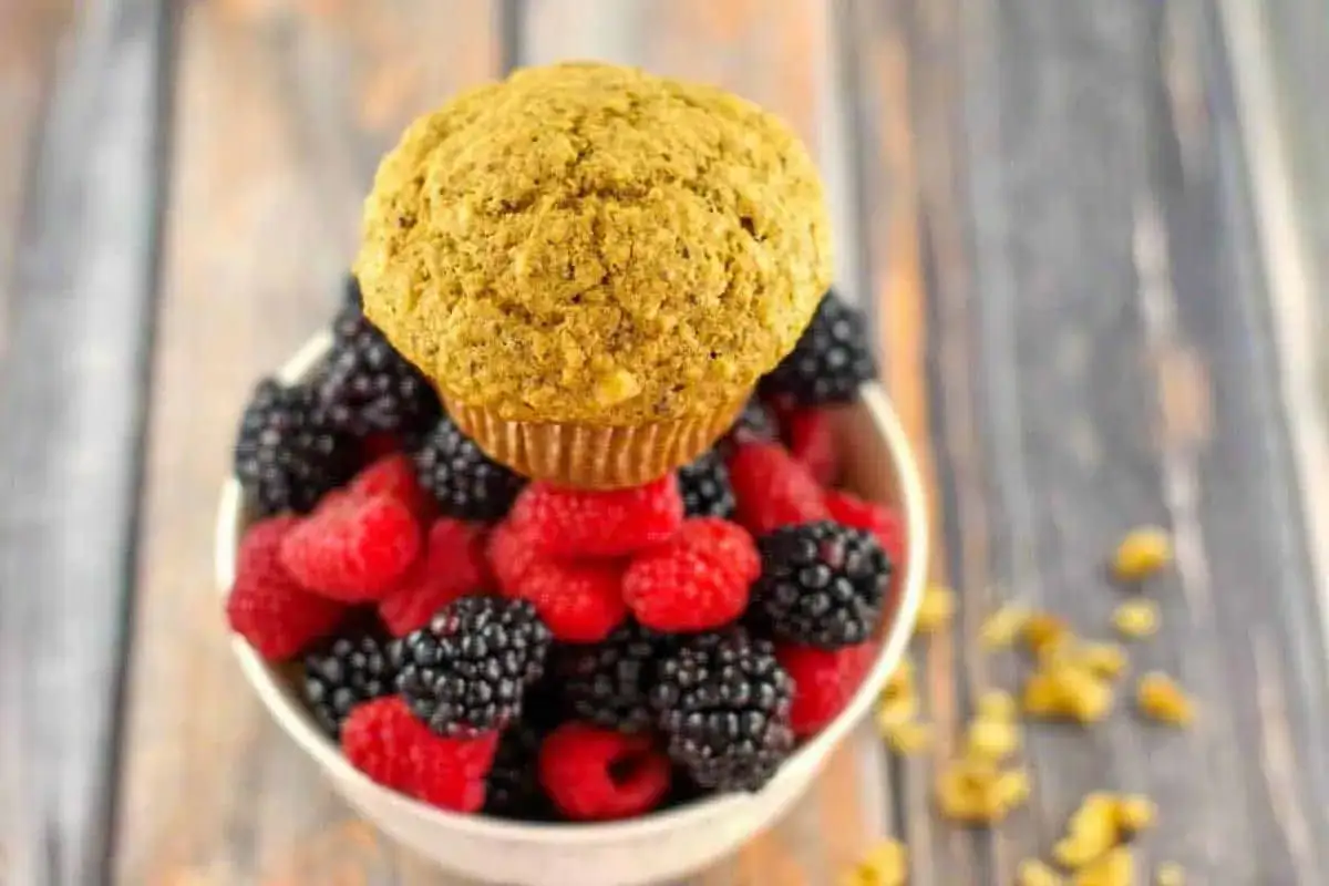 Ein goldbraunes Muffin aus Weizenkleie, reich an Spermidin, thront über einer Schüssel voller frischer Himbeeren und Brombeeren.