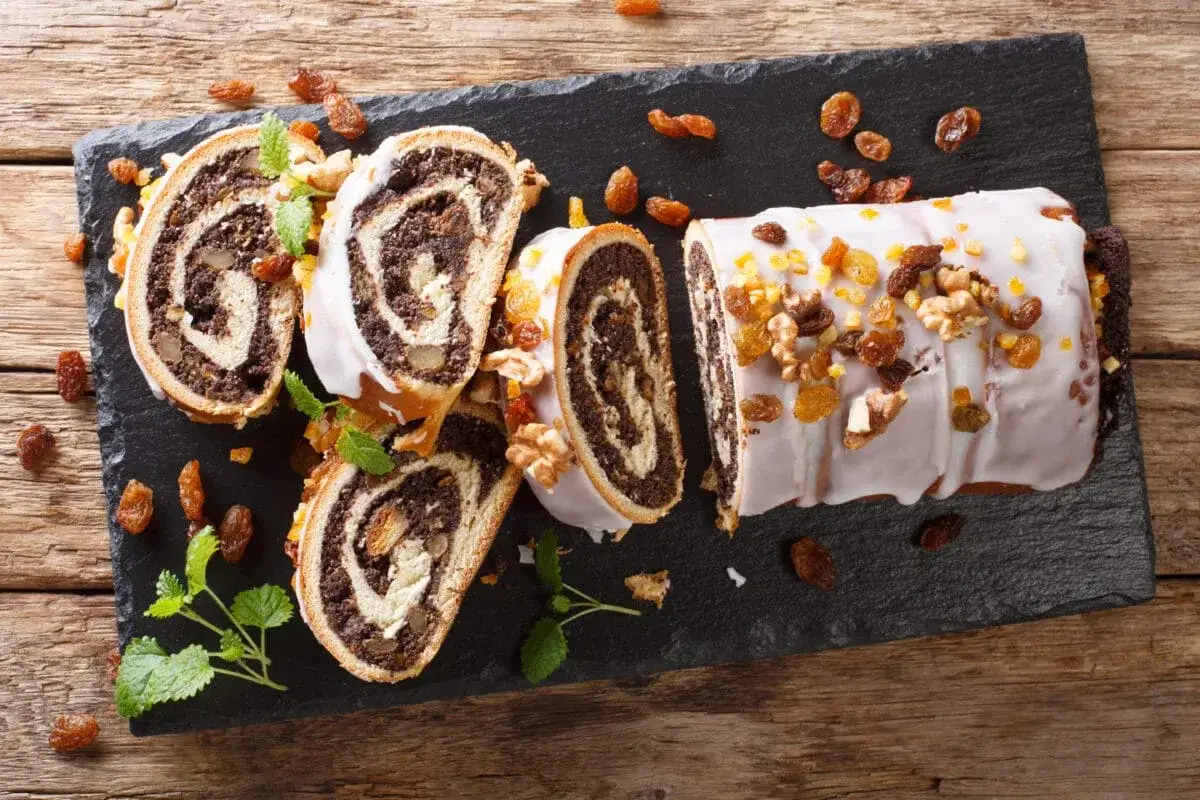 Pyszny makowiec w ciąży, udekorowany bakaliami i orzechami, pokrojony na plastry, leży na czarnej desce.