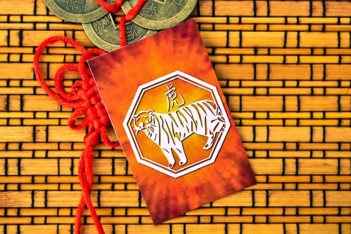 Czerwony sznurek i monety obok kartki z tygrysem, symbolem chińskiego znaku zodiaku.