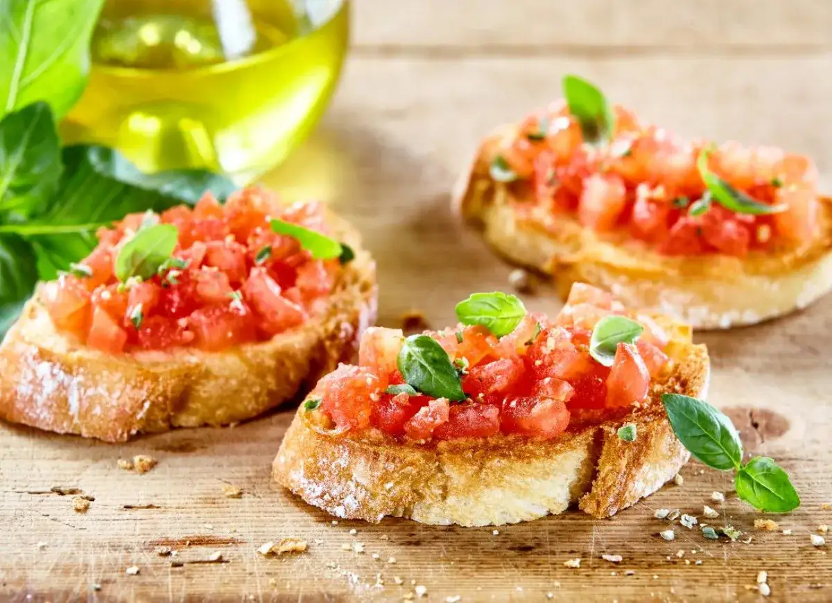 Bruschetta z pomidorami i bazylią, skropiona oliwą, na drewnianej desce.