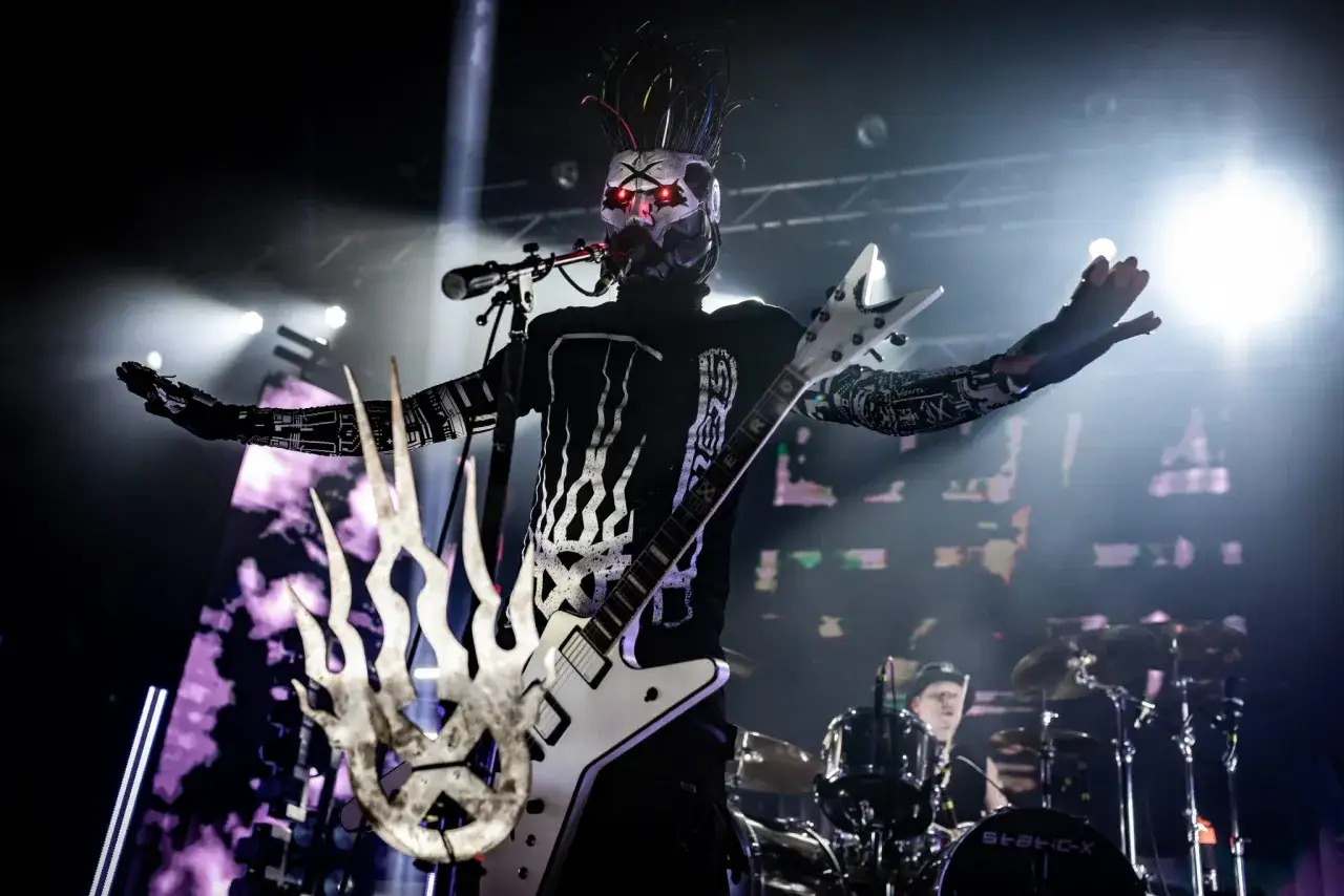 Le chanteur de Static X, masqué et aux yeux rouges, joue de sa guitare blanche en forme d'étoile sur scène.
