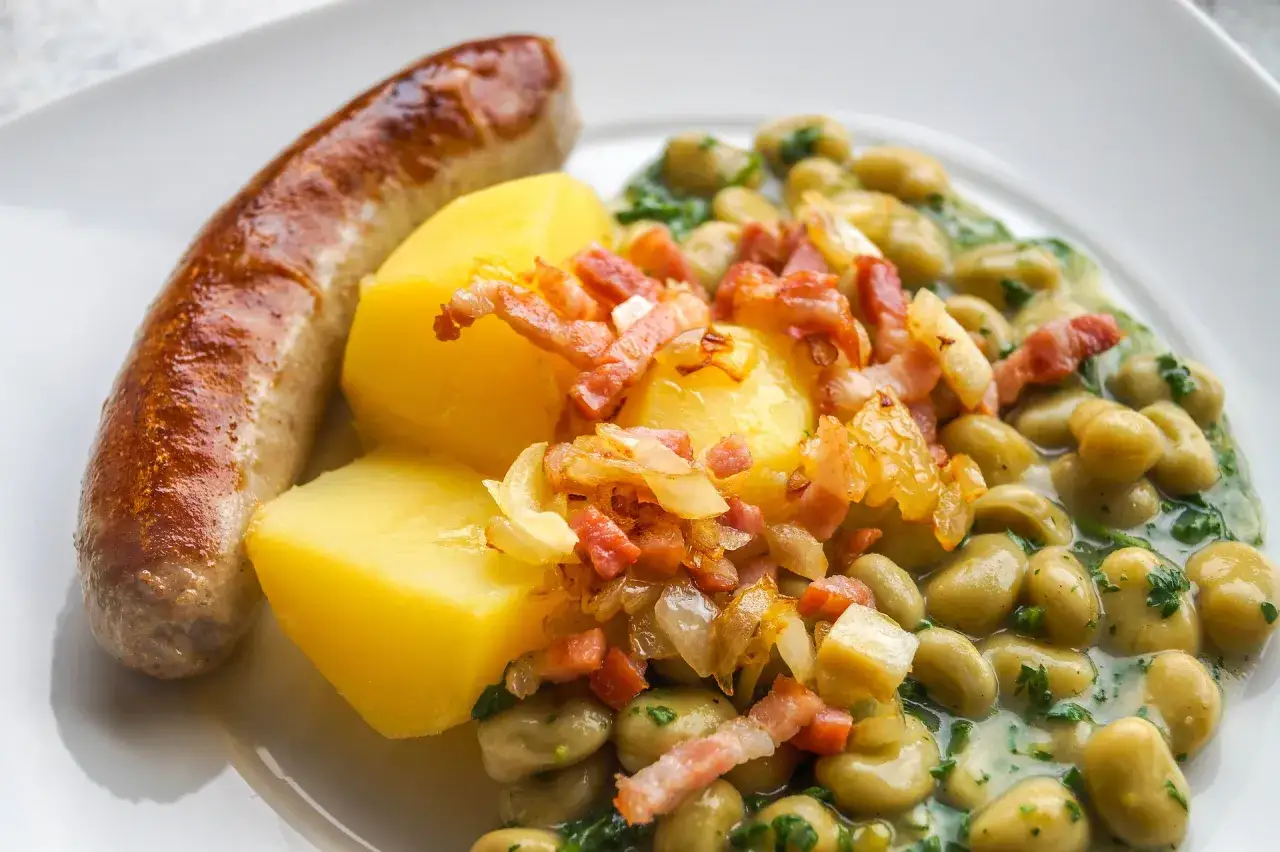 Deftige dicke Bohnen mit Speck und Zwiebeln, dazu Salzkartoffeln und eine Bratwurst. Ein klassisches dicke bohnen rezept.