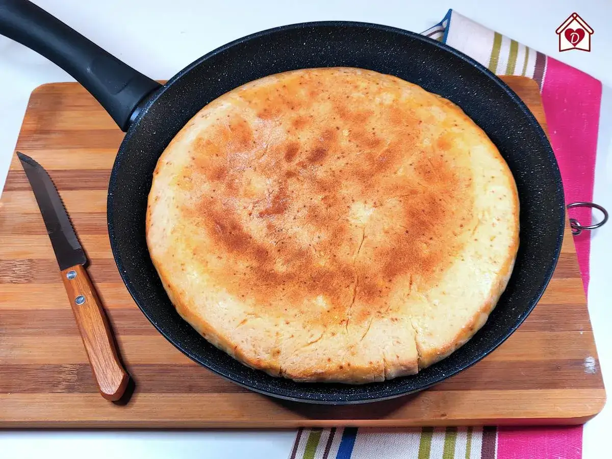 Focaccia senza lievito dorata e soffice in padella, pronta per essere gustata. Accanto, un coltello su un tagliere di legno.