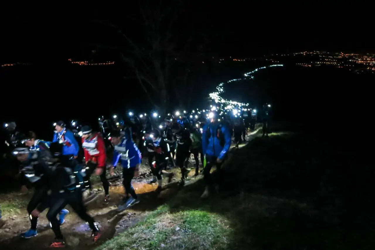 Courseurs nocturnes, frontales allumées, sur un sentier. Un entraînement pour la Saintélyon, avec la ville illuminée au loin.