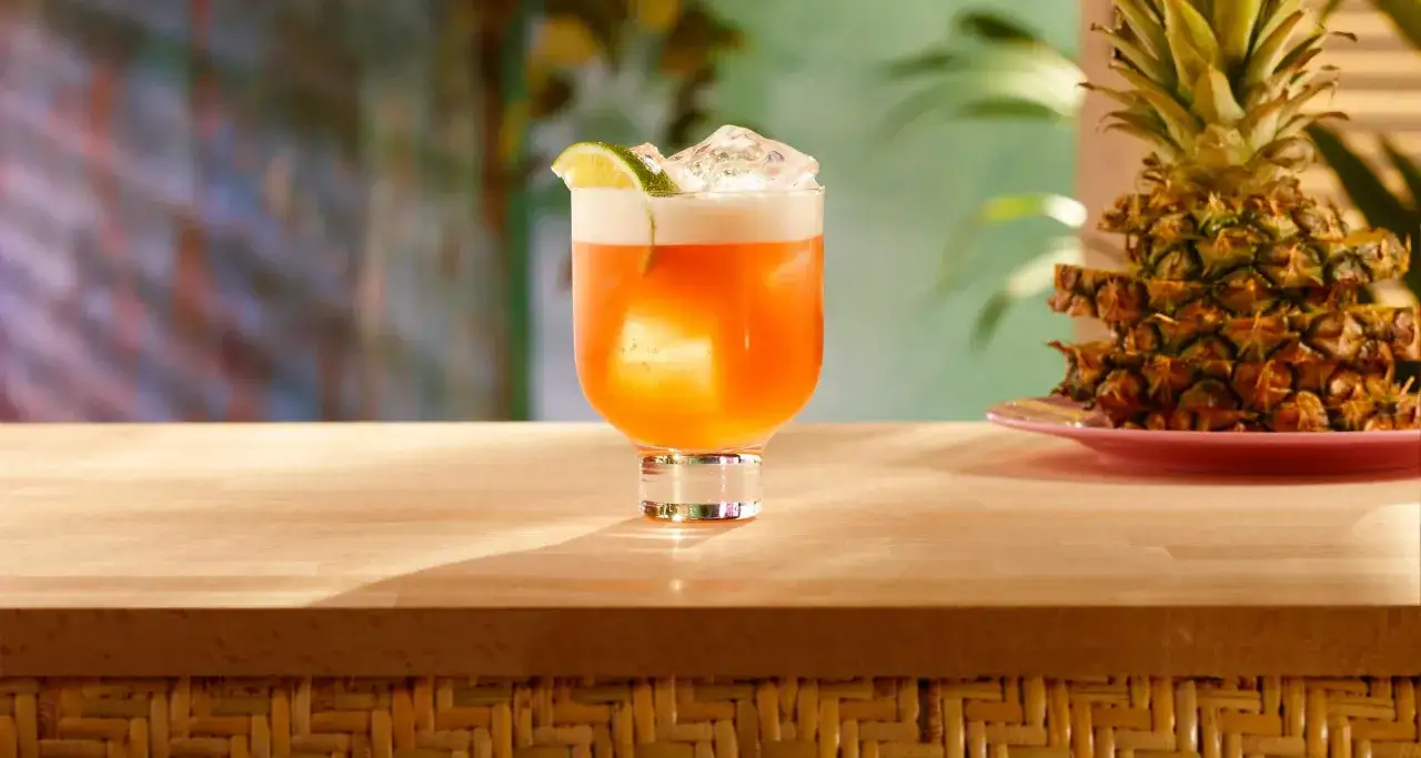 Orzeźwiający drink z rumem Bacardi, lodem i plasterkiem limonki, obok piętrowego ananasa. Idealny na tropikalne popołudnie.
