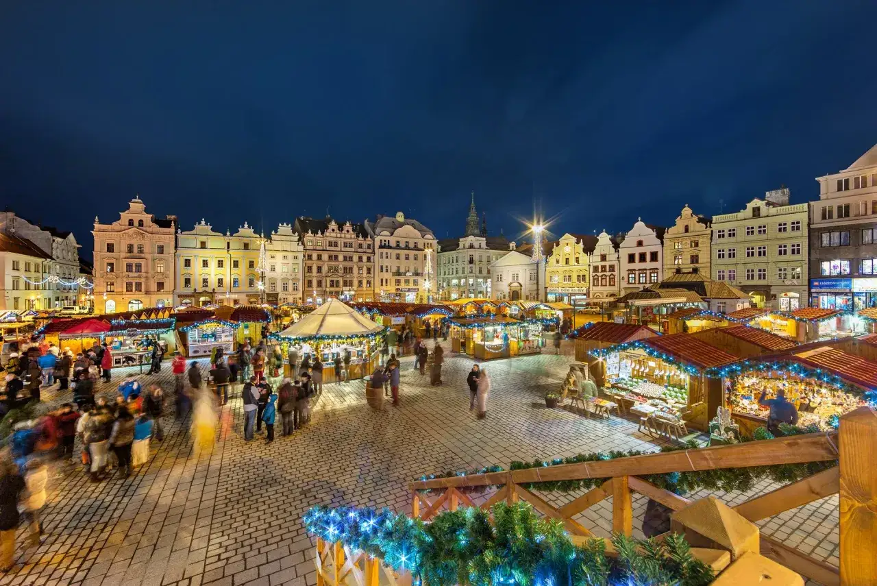 Beleuchtete Buden und gesch&auml;ftiges Treiben auf einem tschechischen Weihnachtsmarkt vor historischer Kulisse.