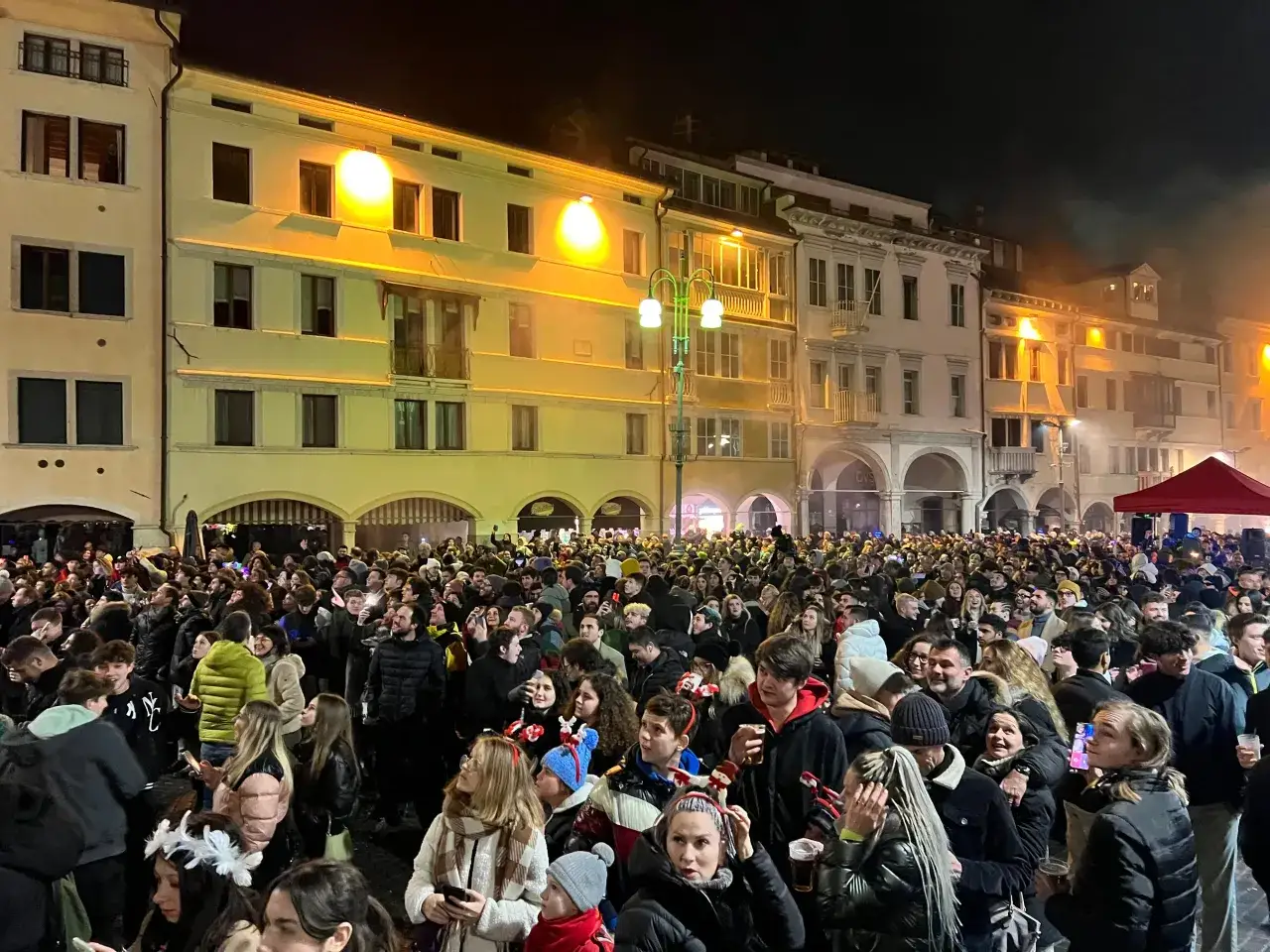 Folla festante in piazza, luci soffuse e l'atmosfera delle canzoni di Capodanno famose nell'aria.