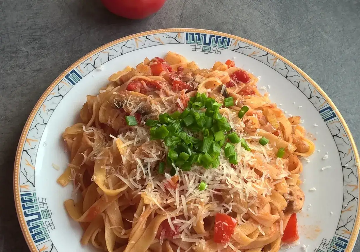 Pyszny makaron z selerem naciowym i pomidorami, posypany parmezanem i szczypiorkiem.