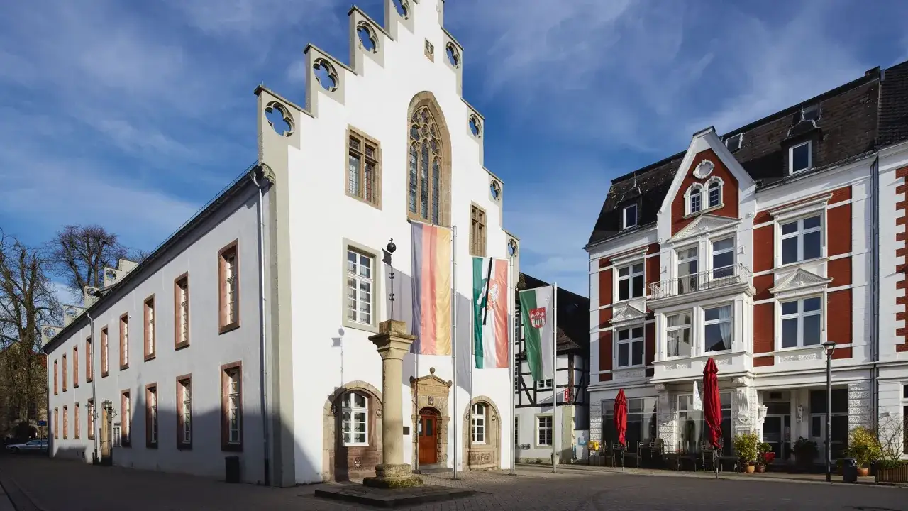 Der Markt in Brakel zeigt ein historisches Rathaus mit deutschen und regionalen Fahnen, daneben ein rotes Backsteingeb&auml;ude mit Caf&eacute;.