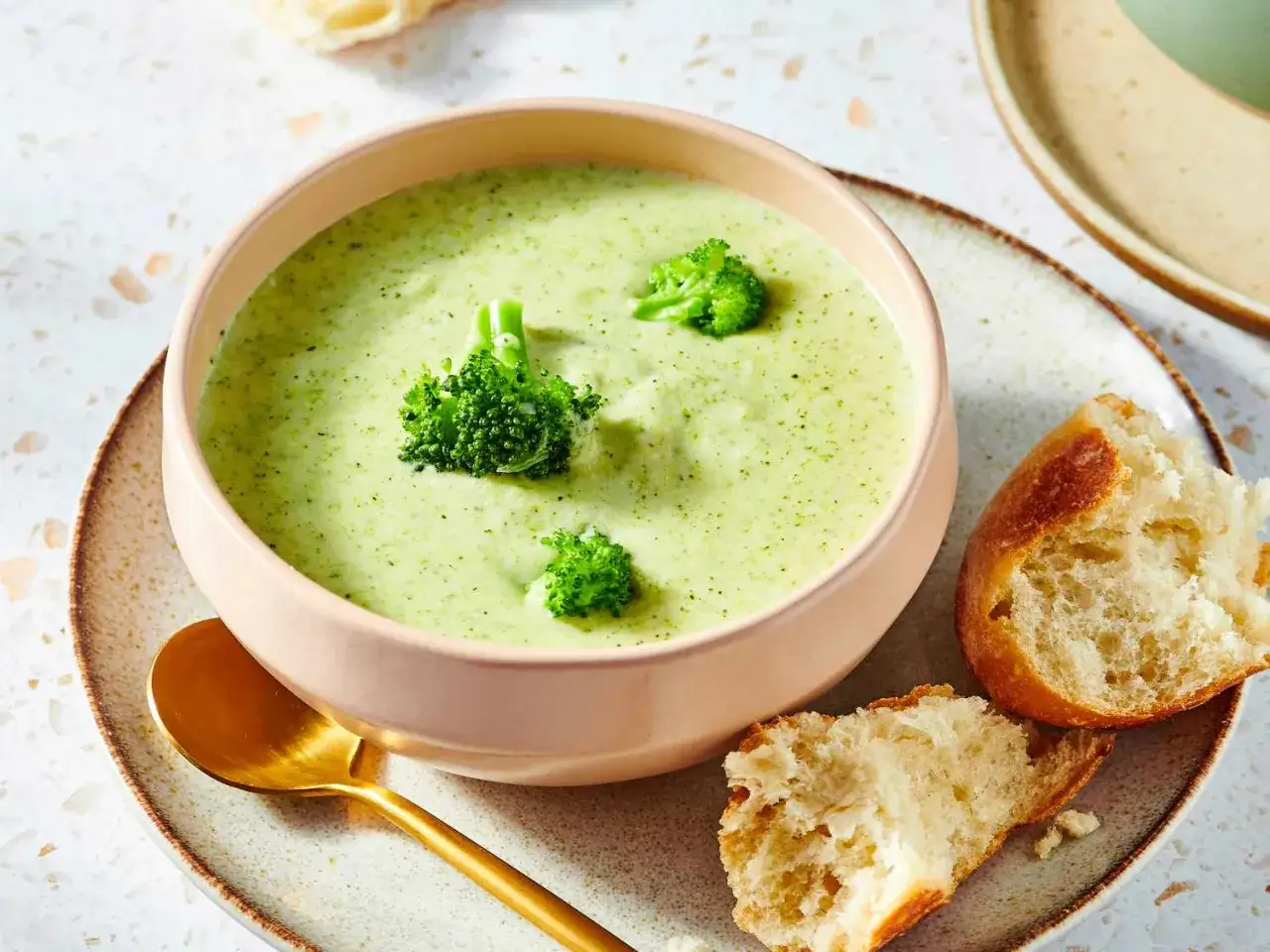 Kr&auml;mig broccolisoppa med potatis, toppad med f&auml;rsk broccoli. Serveras med ett gyllene sked och nybakat br&ouml;d.