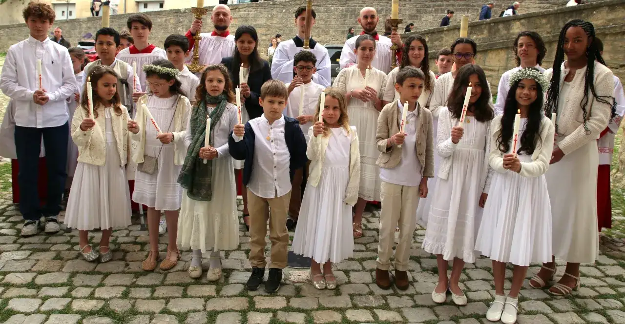 Des enfants en habits blancs tiennent des cierges allumés, prêts à baptiser leur enfant. Une scène solennelle et pleine d'espoir.