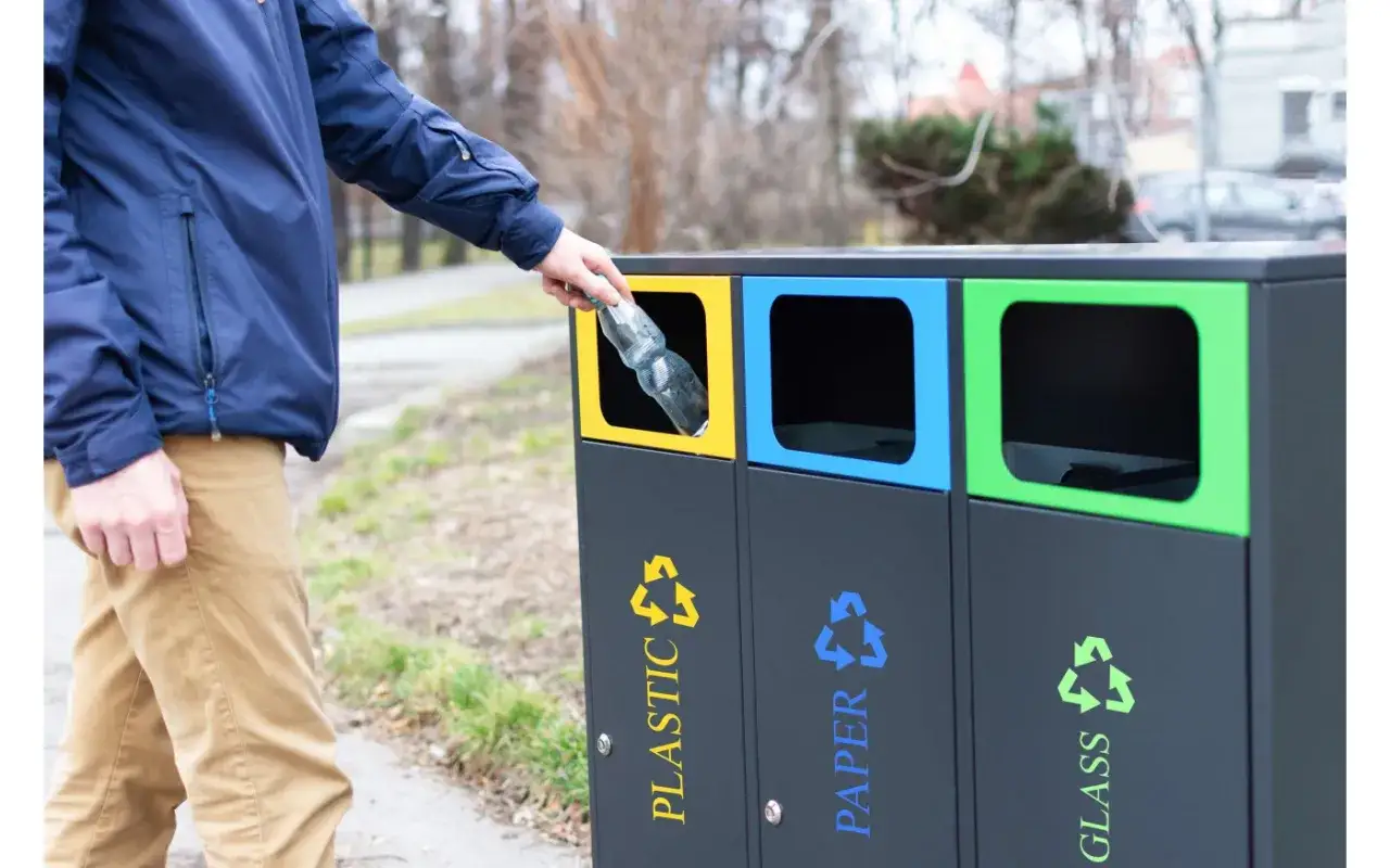 Mężczyzna wrzuca plastikową butelkę do pojemnika na odpady. Segregacja śmieci zapobiega powstawaniu odpadów niebezpiecznych.