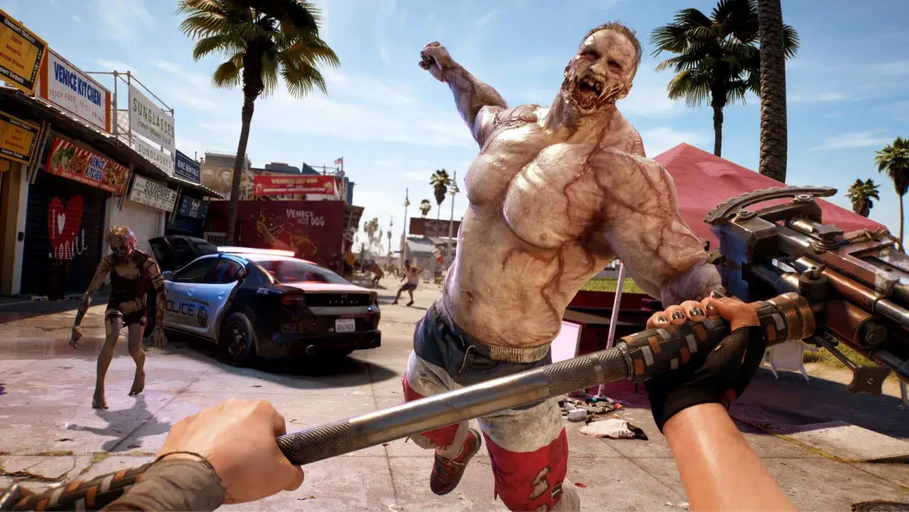 W tej scenie z gry Dead Island 2 czas gry toczy się w słonecznym Venice Beach. Gracz walczy z potężnym zombie, a w tle widać policyjny radiowóz i inne zagrożenia.