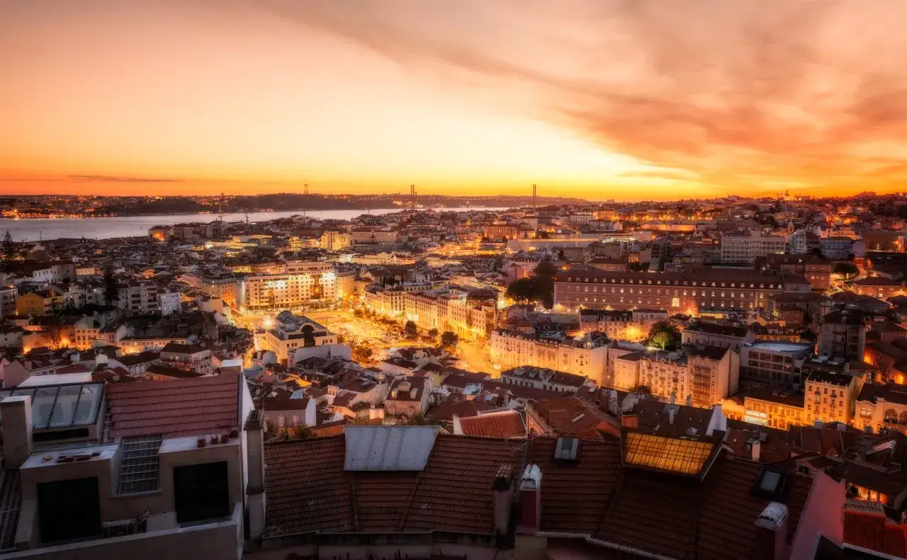 Un espectacular atardecer lisboa ba&ntilde;a la ciudad con tonos naranjas y dorados. Las luces de los edificios comienzan a encenderse, creando un ambiente m&aacute;gico.